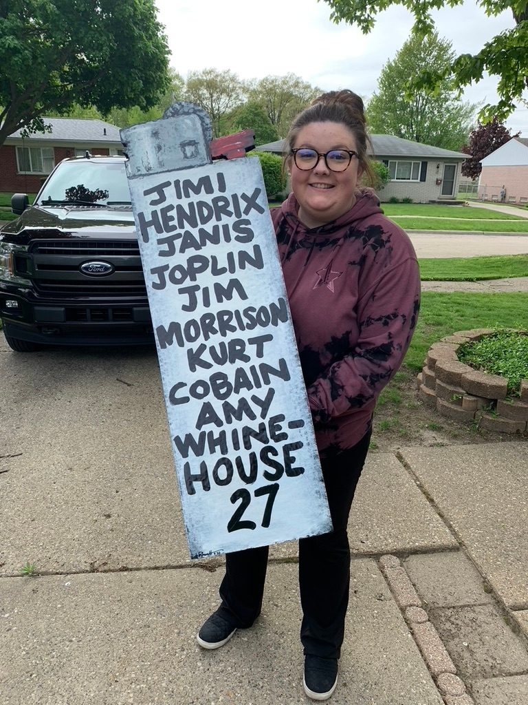 Giant hand-cut and hand-painted lighter lettered with the 27 Club: Jimi Hendrix, Janis Joplin, Jim Morrison, Kurt Cobain and Amy Winehouse, held by a customer in a driveway
