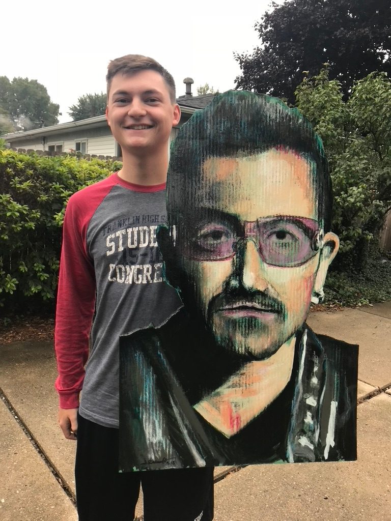 Hand-cut and hand-painted portrait of Bono in tinted glasses, held by a customer outdoors