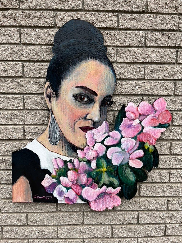 Hand-cut and hand-painted portrait of a woman with a dark updo and silver earring holding a bouquet of pink flowers, on a brick wall